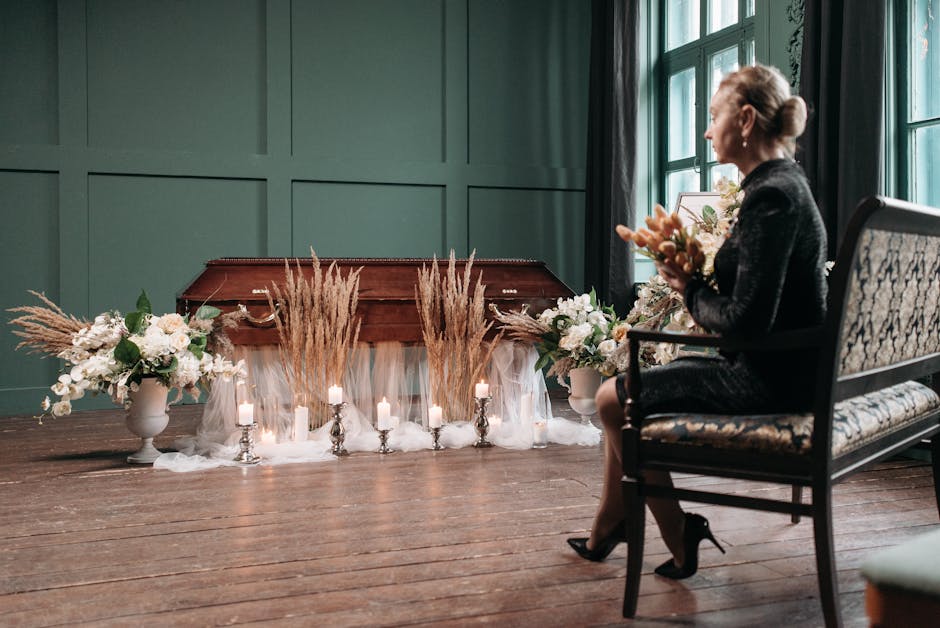 A woman with blonde hair styled in an elegant bun, dressed in a black outfit, is seated on an ornate armchair with a patterned upholstery, holding a small bouquet of flowers. In front of her is a coff