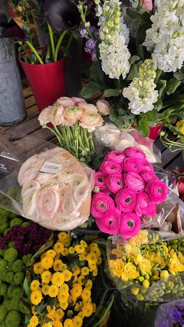 A display of fresh floral arrangements and loose flowers at a flower shop, featuring pink ranunculus, pale pink and white lisianthus, yellow chrysanthemums, and purple and white stock plants. The flow