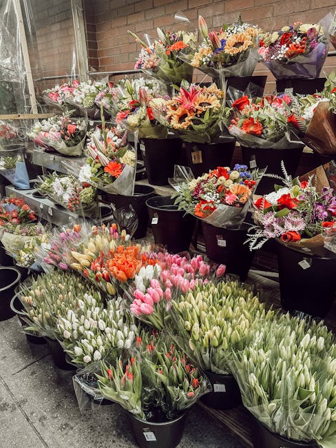 A display of numerous bouquets of fresh flowers arranged on black shelves and in buckets inside a flower shop. The bouquets contain a variety of flowers including pink, white, red, orange, and purple 